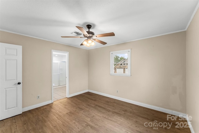 unfurnished bedroom featuring wood finished floors, visible vents, ensuite bath, crown molding, and baseboards