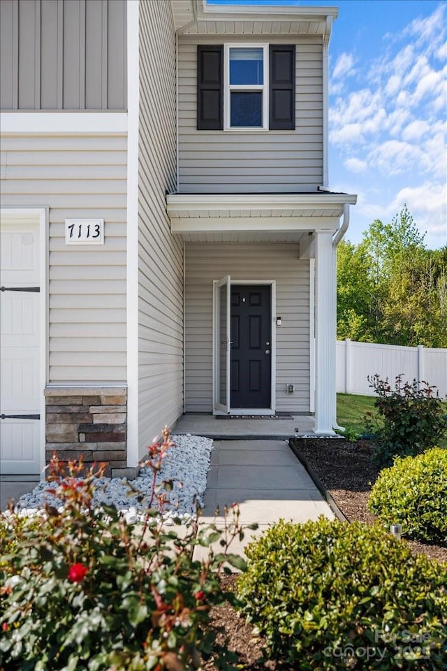 doorway to property featuring stone siding and fence