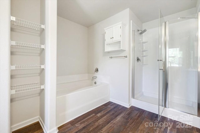 bathroom featuring a shower stall, a spacious closet, wood finished floors, a bath, and baseboards