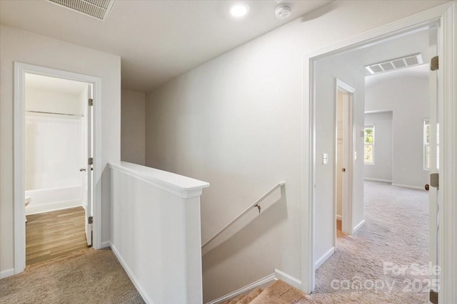 corridor with carpet floors, an upstairs landing, visible vents, and baseboards