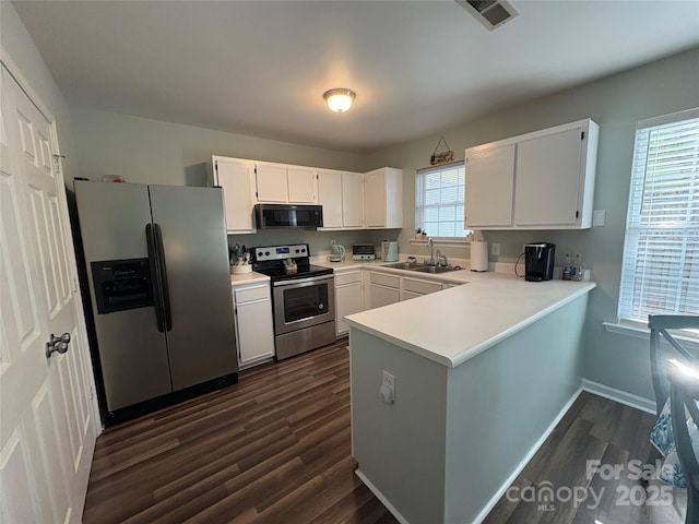 kitchen with a peninsula, a sink, dark wood-style flooring, visible vents, and appliances with stainless steel finishes