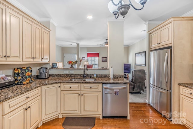 kitchen featuring stainless steel appliances, light wood-style flooring, a sink, ornamental molding, and cream cabinets