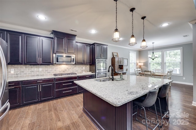 kitchen featuring a sink, light wood finished floors, backsplash, and stainless steel appliances