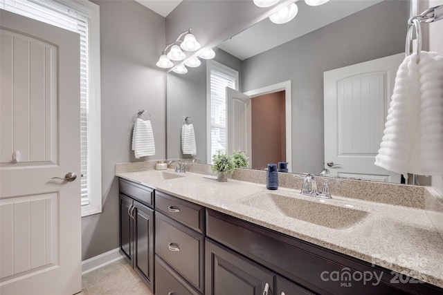 bathroom featuring baseboards, a sink, tile patterned floors, and double vanity
