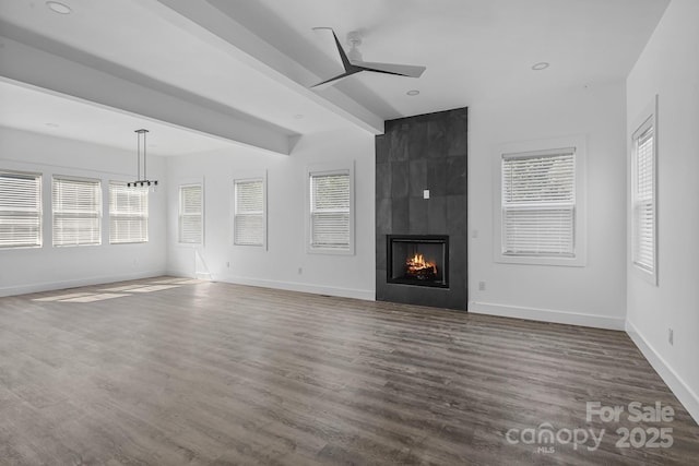 unfurnished living room with wood finished floors, ceiling fan, a large fireplace, baseboards, and beam ceiling