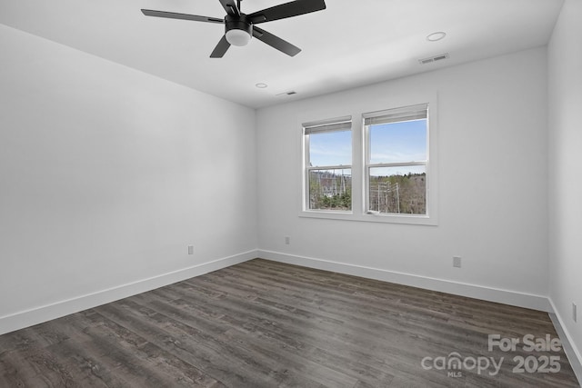 spare room with dark wood-type flooring, visible vents, a ceiling fan, and baseboards