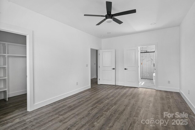 unfurnished bedroom with a spacious closet, baseboards, ensuite bath, and wood finished floors