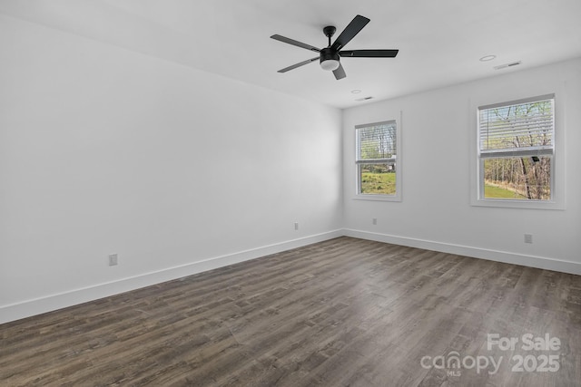 empty room with dark wood-type flooring, baseboards, visible vents, and a wealth of natural light