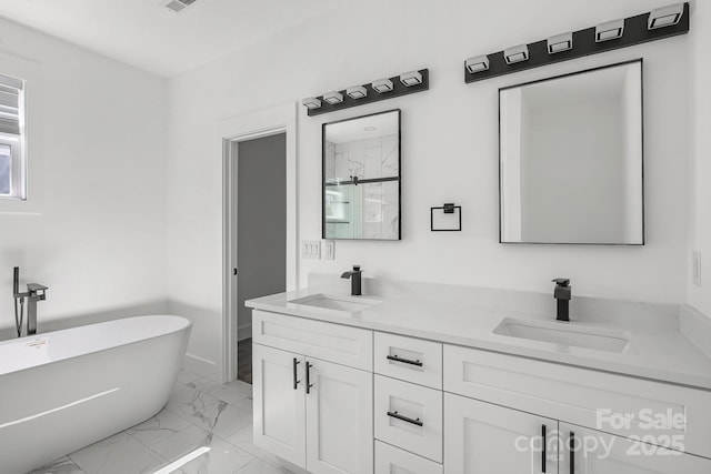 bathroom with marble finish floor, a freestanding bath, a sink, and double vanity