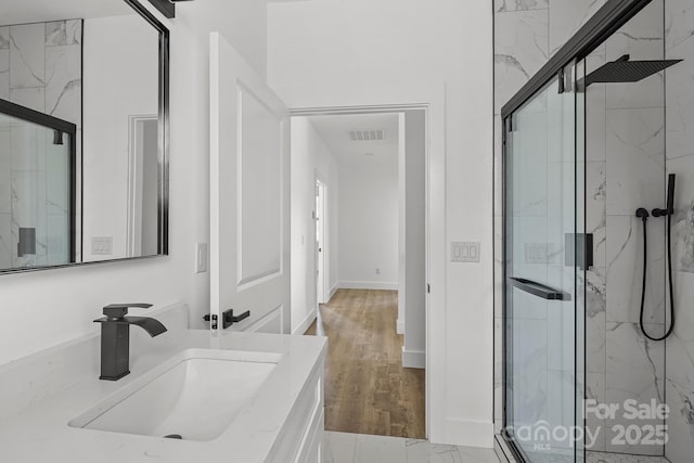 full bath featuring wood finished floors, visible vents, vanity, a marble finish shower, and baseboards