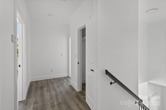 hall featuring dark wood-type flooring, baseboards, and an upstairs landing