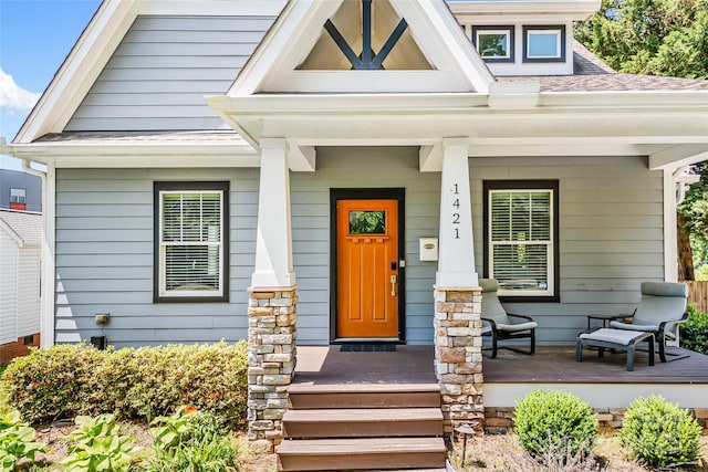doorway to property with covered porch and a shingled roof