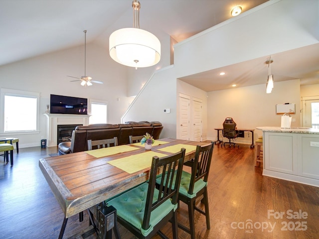 dining area with high vaulted ceiling, dark wood-type flooring, ceiling fan, a fireplace, and baseboards