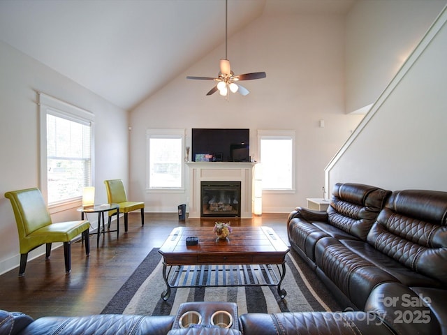 living area featuring wood finished floors, healthy amount of natural light, a glass covered fireplace, ceiling fan, and high vaulted ceiling