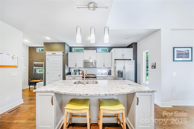 kitchen with appliances with stainless steel finishes, a sink, a breakfast bar, a kitchen island with sink, and light wood-type flooring