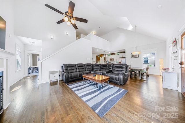 living area with high vaulted ceiling, ceiling fan, and wood finished floors
