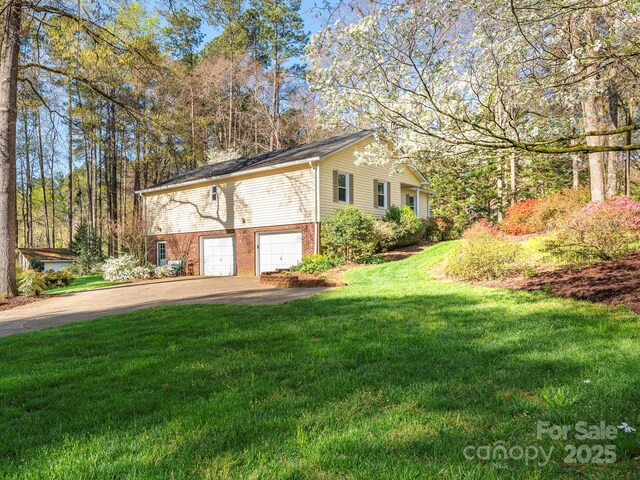 view of side of property with brick siding, a yard, an attached garage, and concrete driveway