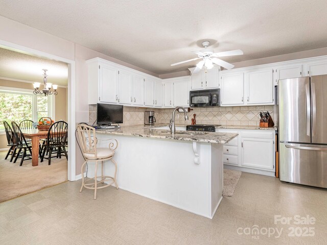 kitchen featuring a sink, freestanding refrigerator, black microwave, white cabinetry, and ceiling fan with notable chandelier