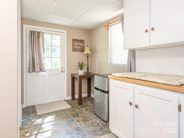 entryway featuring stone finish floor, a paneled ceiling, and baseboards