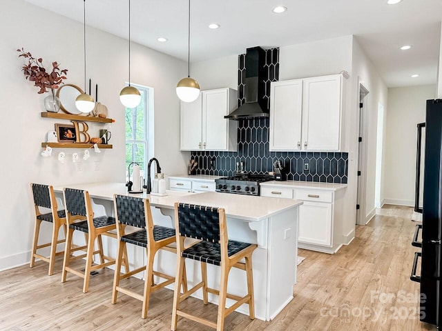 1123 Fern Hill Rd, Mooresville, NC 28117 - kitchen featuring a breakfast bar area, wall chimney exhaust hood, backsplash, light wood-type flooring, and stove