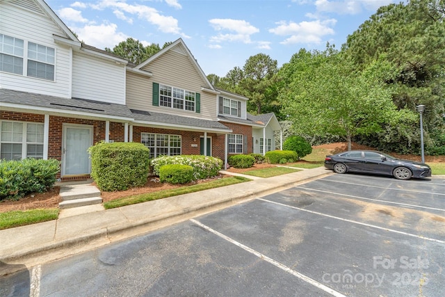 multi unit property with uncovered parking, roof with shingles, and brick siding