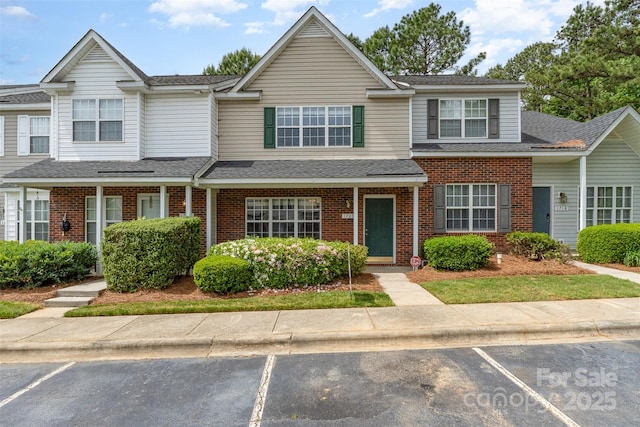 townhome / multi-family property featuring brick siding, uncovered parking, and roof with shingles