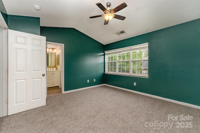 unfurnished bedroom featuring connected bathroom, carpet flooring, baseboards, visible vents, and lofted ceiling