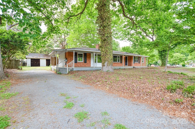 ranch-style home featuring an outdoor structure, a chimney, covered porch, driveway, and brick siding