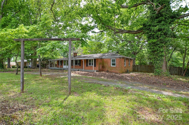 view of front facade featuring a chimney, a porch, brick siding, fence, and a front lawn