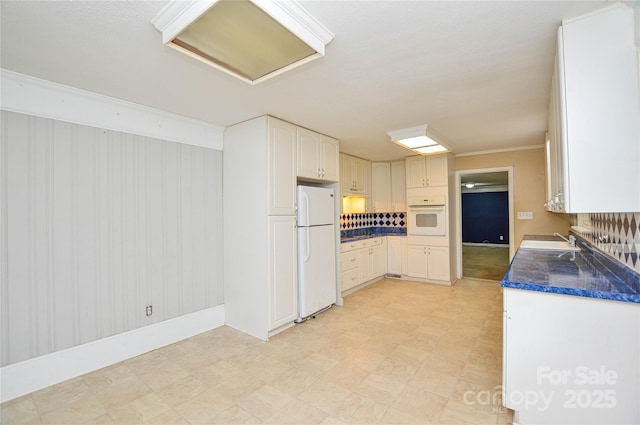 kitchen featuring a sink, dark countertops, baseboards, light floors, and white appliances