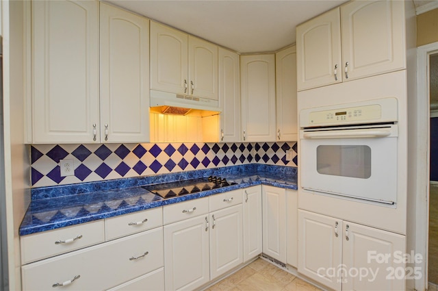 kitchen with white oven, black electric stovetop, under cabinet range hood, and dark countertops