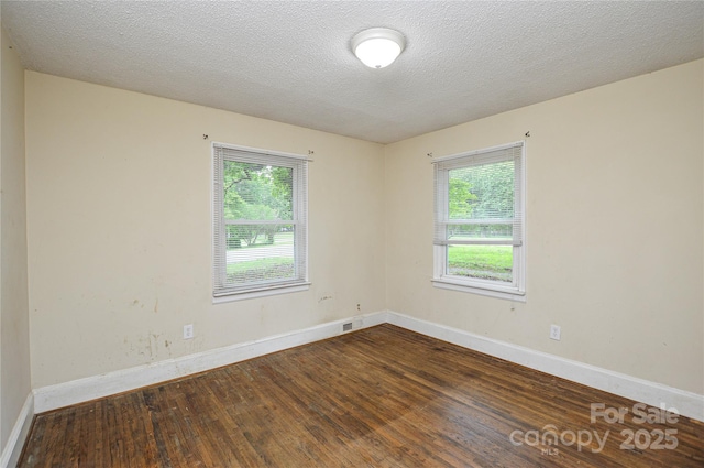 spare room featuring baseboards, a healthy amount of sunlight, and dark wood-type flooring