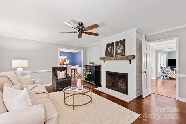 living room featuring crown molding, baseboards, a brick fireplace, wood finished floors, and a ceiling fan