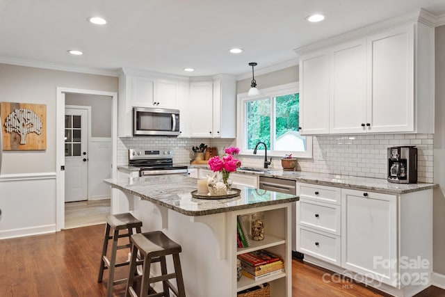 kitchen featuring decorative backsplash, white cabinets, appliances with stainless steel finishes, dark wood-style flooring, and a kitchen bar