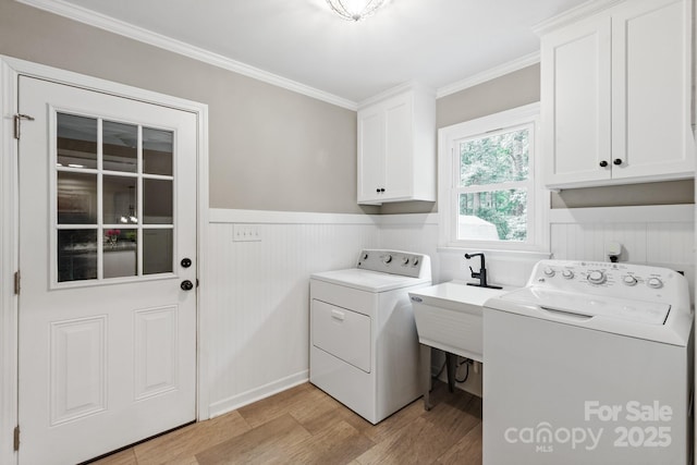 laundry area with independent washer and dryer, light wood-style flooring, a wainscoted wall, ornamental molding, and cabinet space