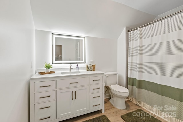 full bathroom featuring a shower with shower curtain, toilet, vaulted ceiling, wood finished floors, and vanity