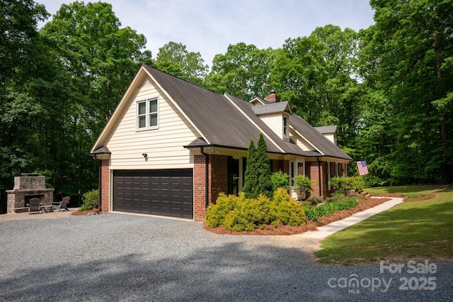 view of front of house featuring a chimney, gravel driveway, brick siding, exterior fireplace, and roof with shingles