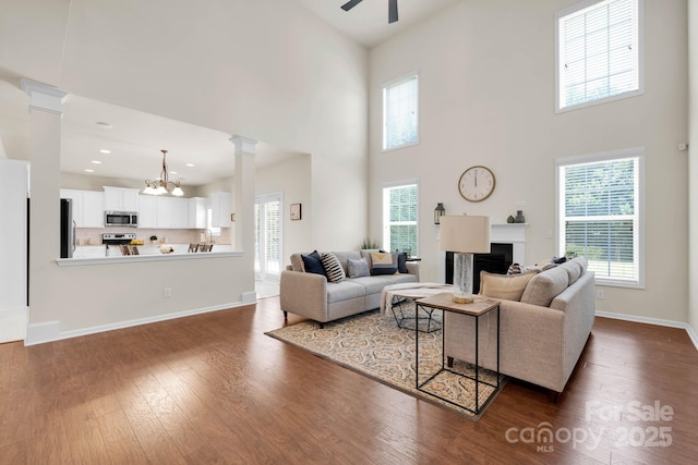 living area with ceiling fan with notable chandelier, dark wood-style floors, a fireplace, and ornate columns