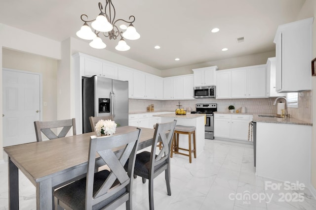 kitchen featuring a sink, marble finish floor, an inviting chandelier, stainless steel appliances, and a kitchen island