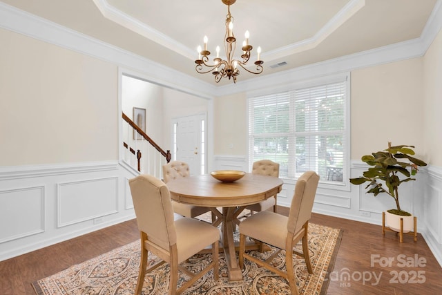 dining area featuring a decorative wall, wood finished floors, stairs, a raised ceiling, and a notable chandelier