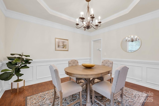 dining room featuring dark wood-type flooring, ornamental molding, a notable chandelier, and a tray ceiling
