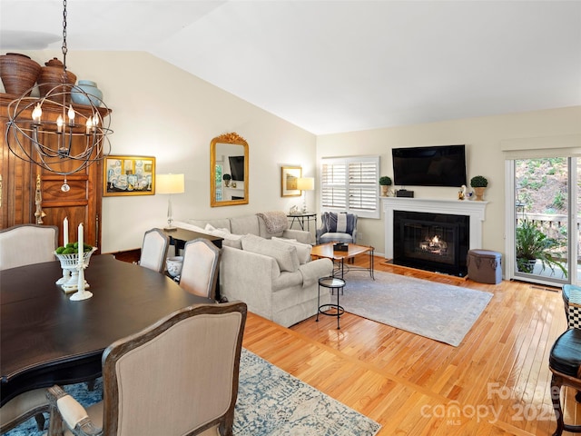 living area featuring lofted ceiling, wood finished floors, an inviting chandelier, and a fireplace with flush hearth