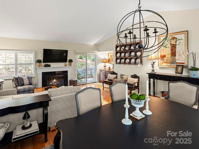dining room with a chandelier, lofted ceiling, a glass covered fireplace, and wood finished floors