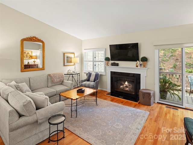 living area with vaulted ceiling, visible vents, wood finished floors, and plenty of natural light