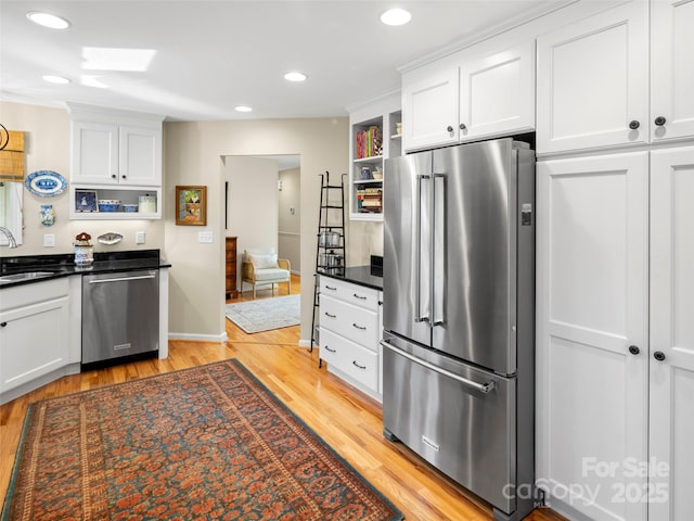 kitchen featuring stainless steel appliances, a sink, light wood-type flooring, dark countertops, and open shelves