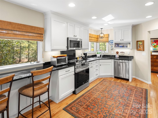 kitchen with white cabinets, light wood finished floors, stainless steel appliances, dark countertops, and a sink