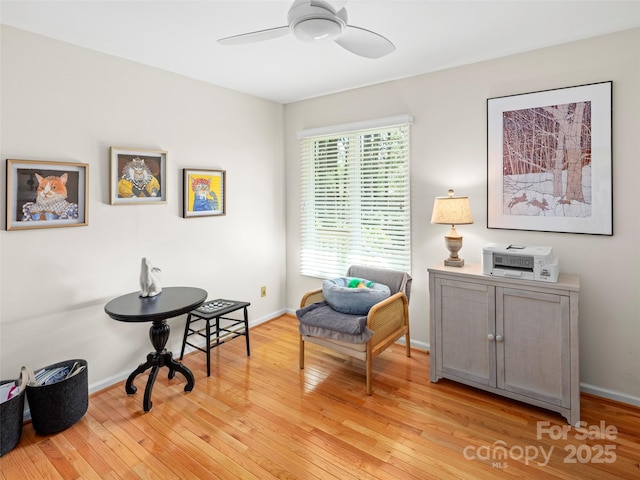 living area with baseboards, a ceiling fan, and light wood-type flooring