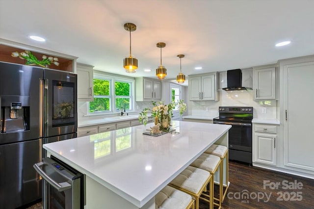 kitchen with wall chimney exhaust hood, a sink, stainless steel fridge, black electric range oven, and light countertops