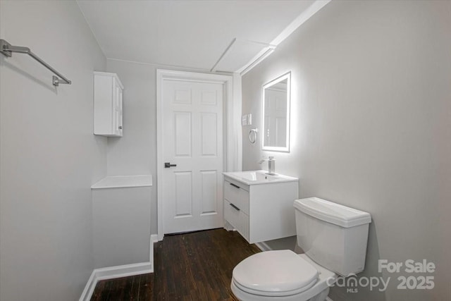 half bathroom with baseboards, wood finished floors, toilet, and vanity
