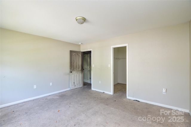 unfurnished bedroom with a closet, a spacious closet, carpet, and baseboards
